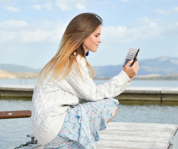 a woman holding a phone on the side of a lake